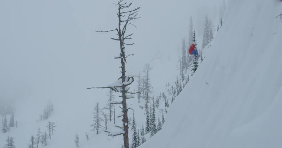 A snowboarder jumps off the top of a steep mountain slope and falls several meters before landing in deep snow