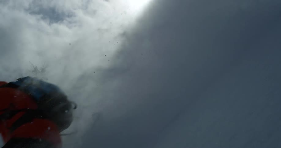 A person with a backpack skiing down a mountain with the sky and clouds in the background