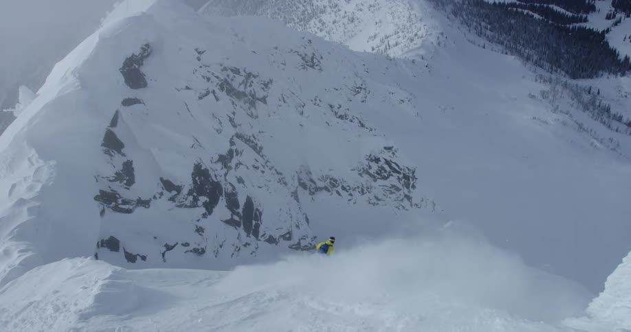 A person in yellow and blue snow gear is skiing down a steep snowy slope