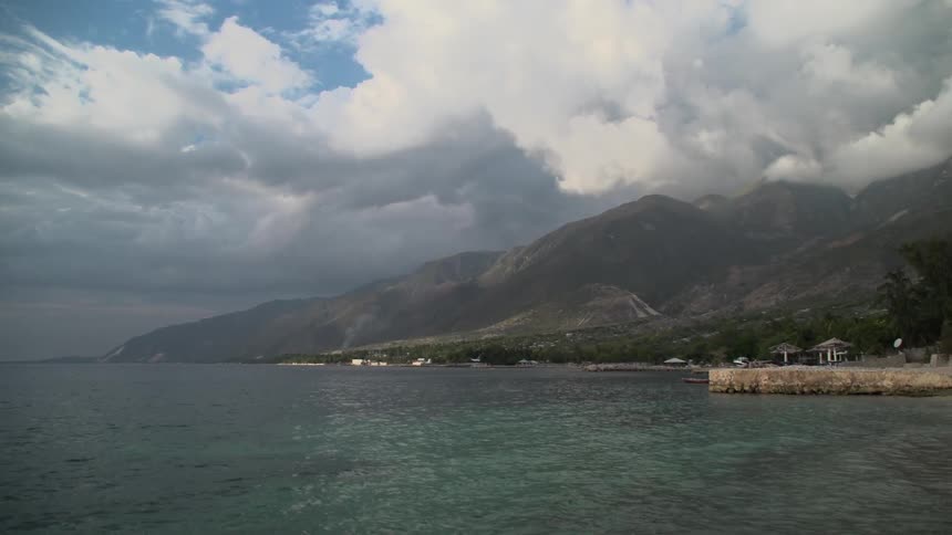 Water laps at a shore and clouds hang over mountains