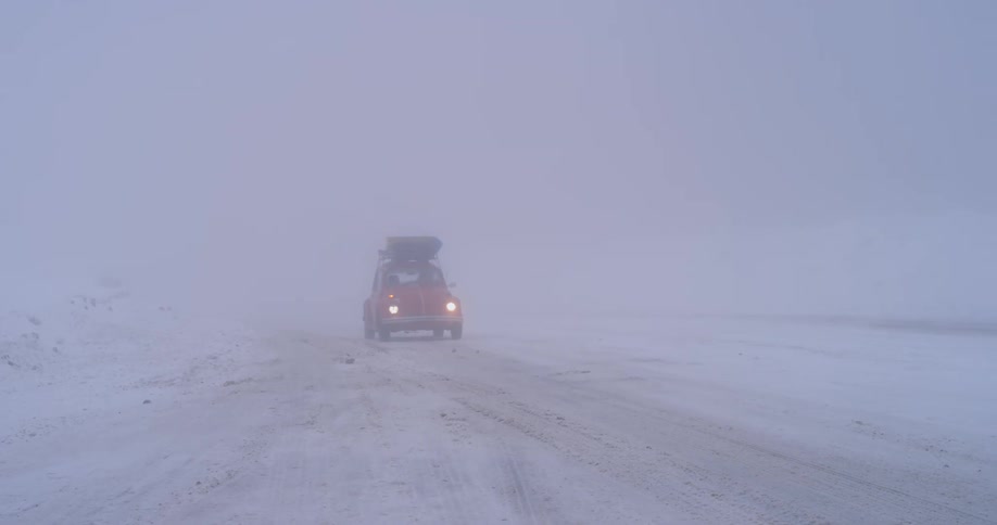 A car with headlights driving in a blizzard on a snow covered road