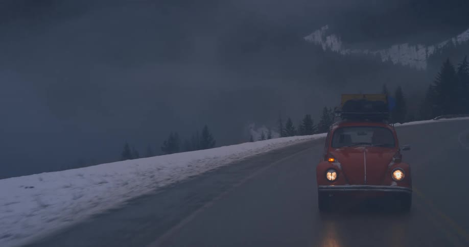 A vehicle with luggage strapped to a roof rack travels along an icy road in the mountains