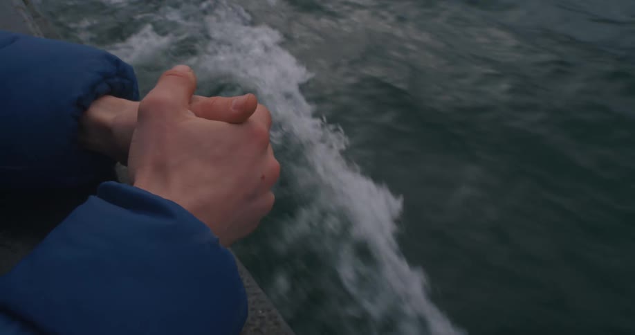 Hands clasped over boat railing above wake in water