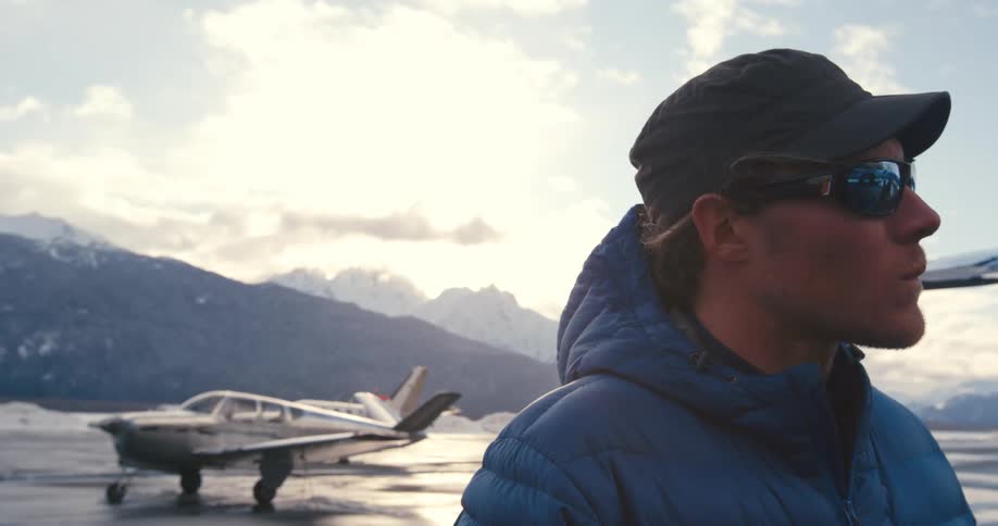 Man stands on tarmac a distance from parked airplane with mist covered mountains in background