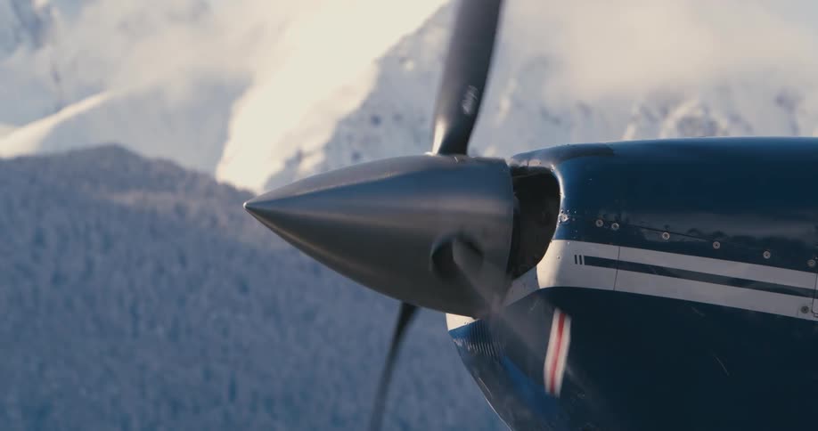 An airplane propeller rotating with a mountain range the sky and clouds in the background
