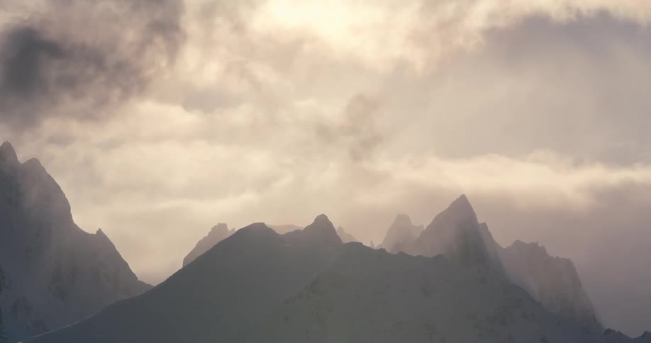 A mountain range covered in snow with the sky and clouds in the background