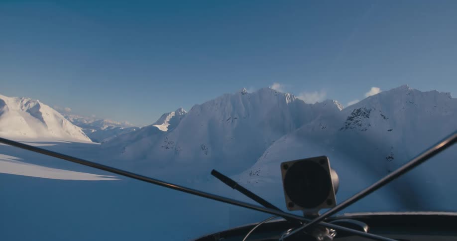 View from front of small aircraft flying over snow covered mountains
