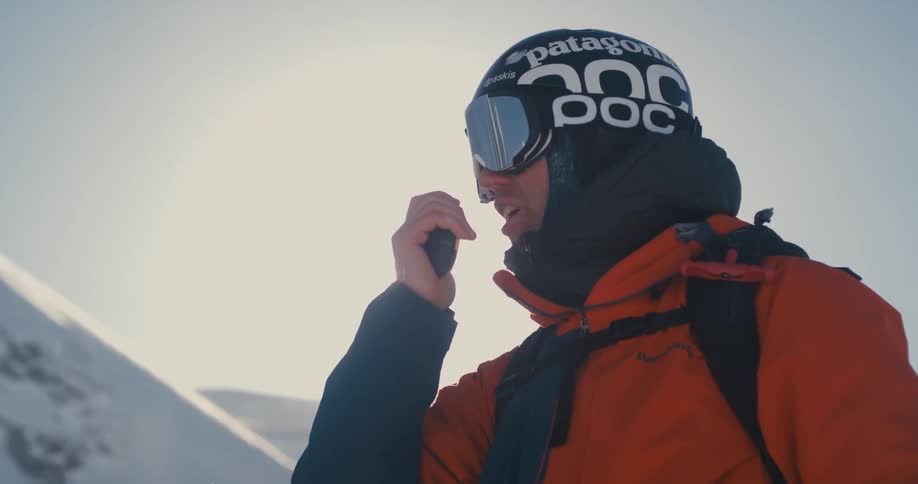A skier uses a walkie talkie to talk to someone in the distance
