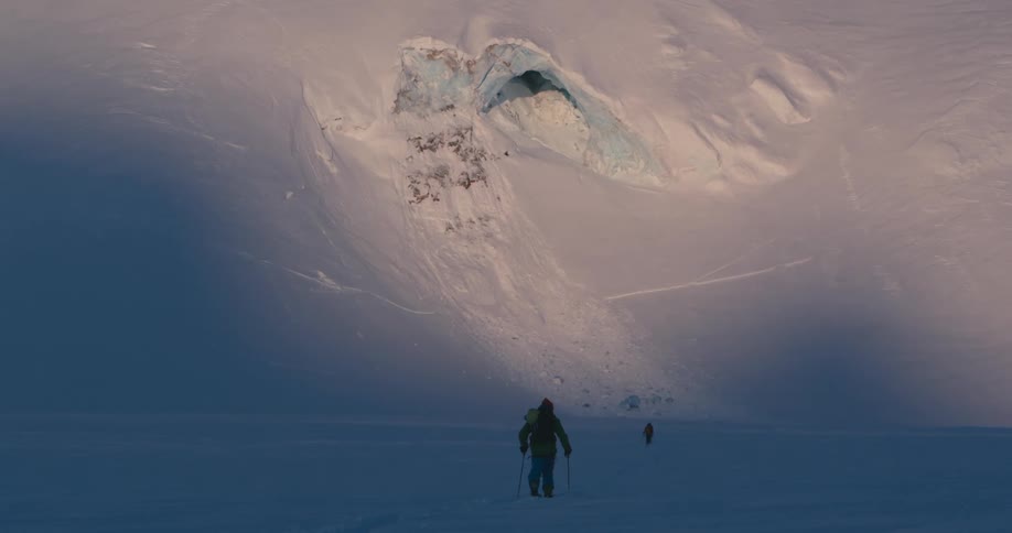 Two people trekking in the snow near a mountain slope