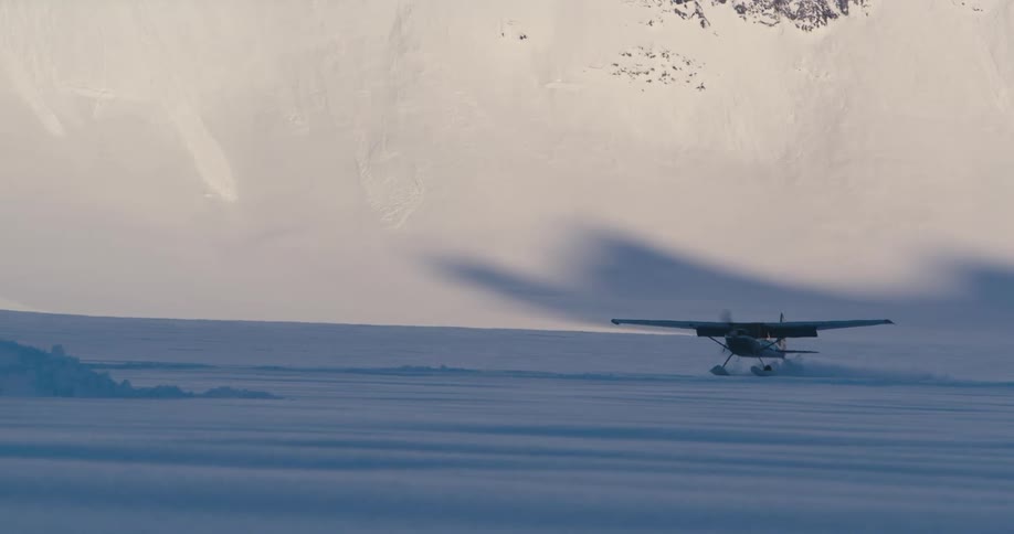 A airplane lands in a snowy field at the base of a mountain