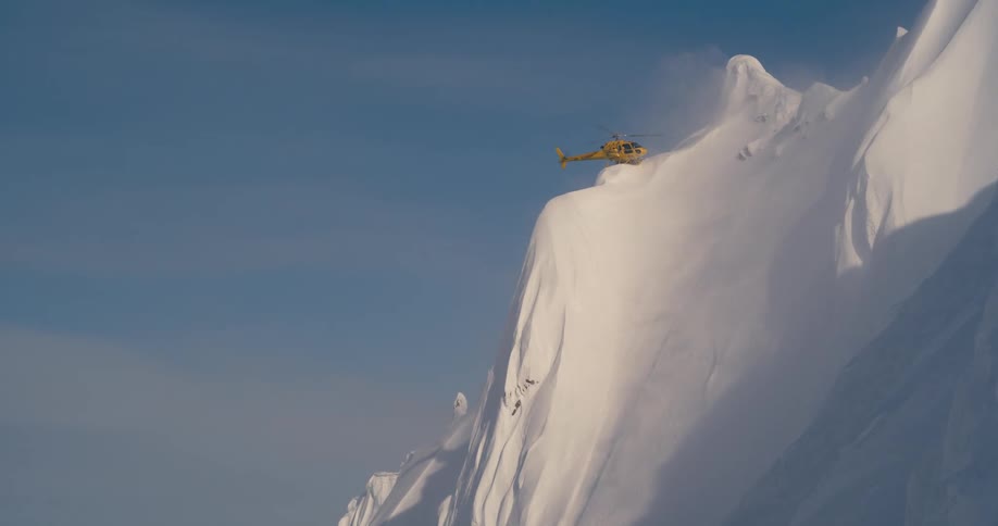 A helicopter flies over snowy mountains in the wilderness