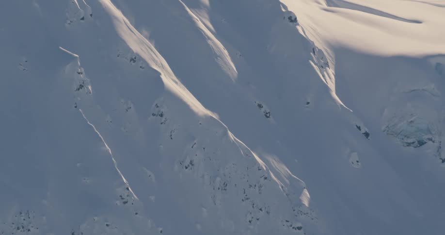 Snow covers steep mountain slope as sun highlights parts and casts other parts into shadow