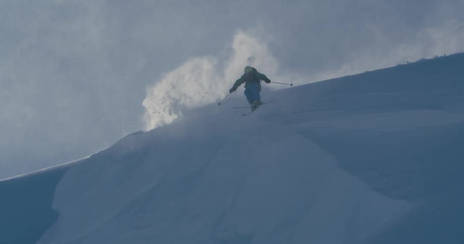 Skier jumps down a cliff landing on snow in the mountains