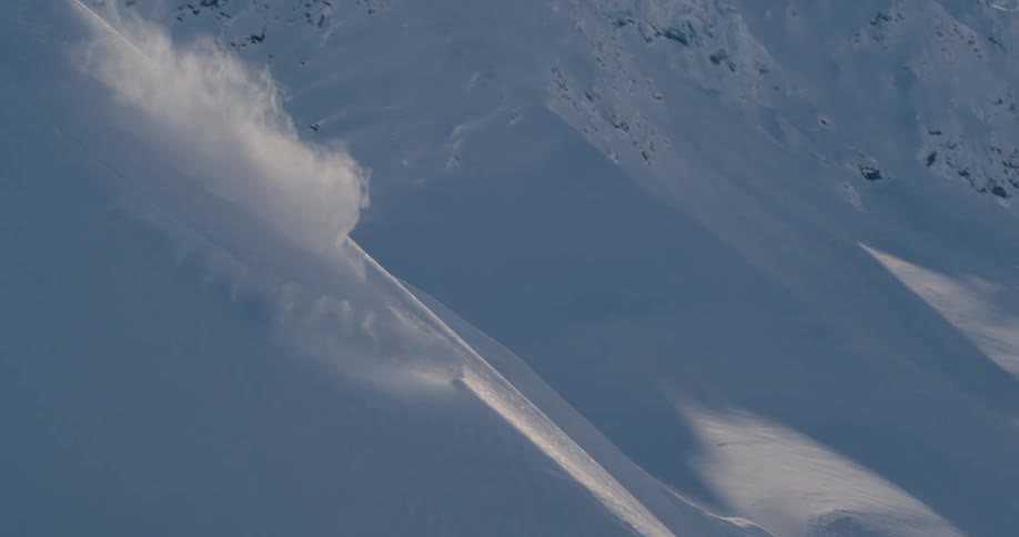 A person on a snowboard going down a snowy slope with a mountain range and the sky in the background