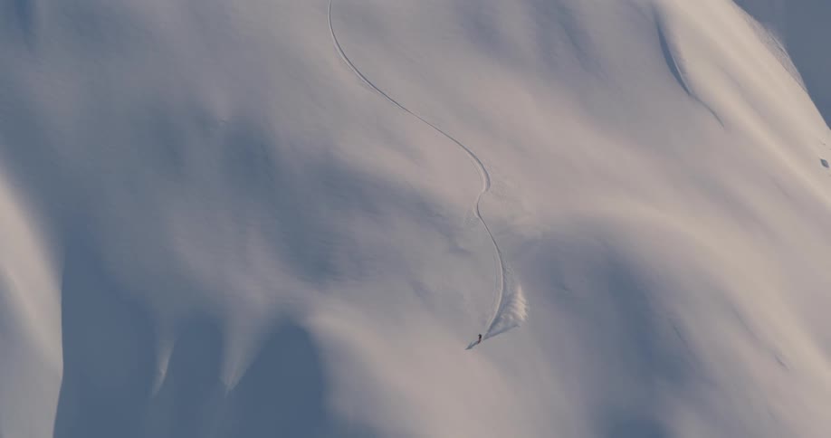 An aerial view of a skier gliding down a snowy mountainside