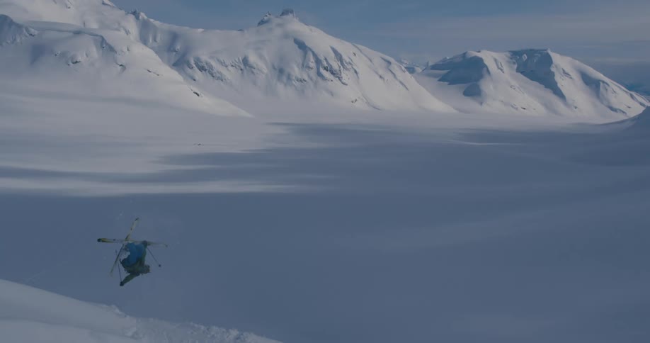 A person with a backpack skiing and jumping with a mountain range and the sky in the background