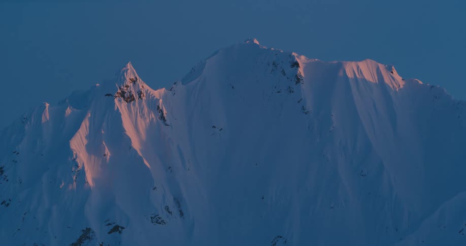 A mountain range covered in snow with the sky and clouds in the background