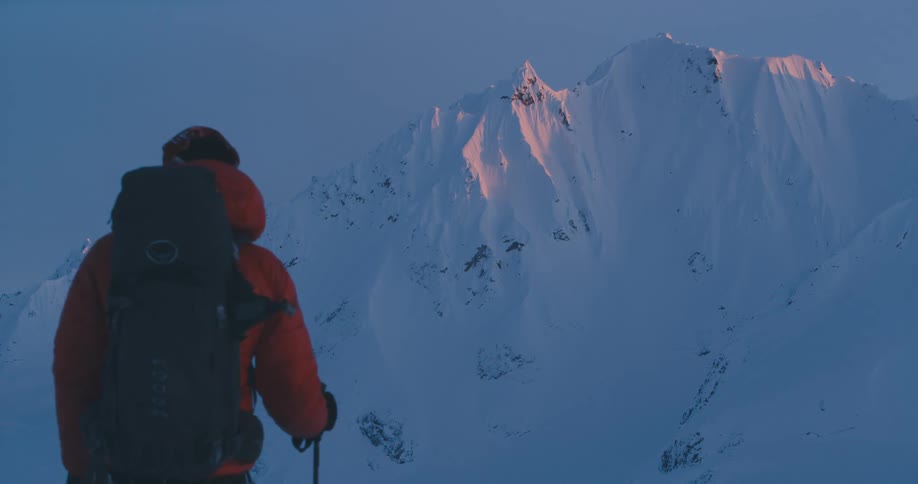 A hiker pauses for a moment before continuing their hike through snowy mountains in the evening