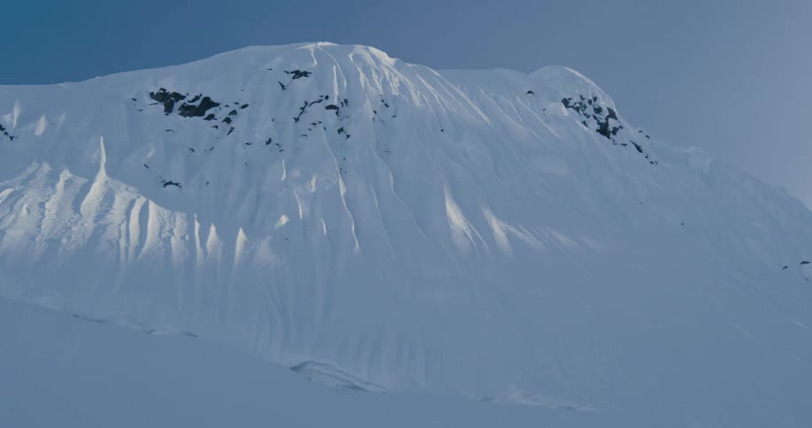 A snow covered mountain with sunlight with the sky and clouds in the background