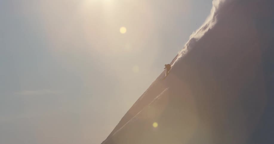 A skier descends a steep mountain slope as the sun shines overhead