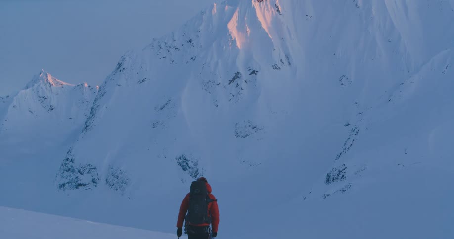 A skier uses ski poles to slowly push themselves across a snowy hill in the mountains during the day