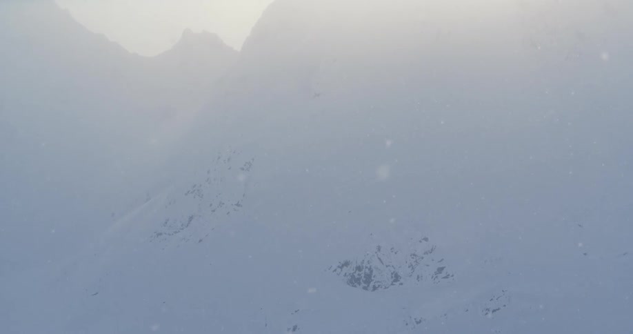 Sunlight filter through the light snowfall over an encampent in the mountains