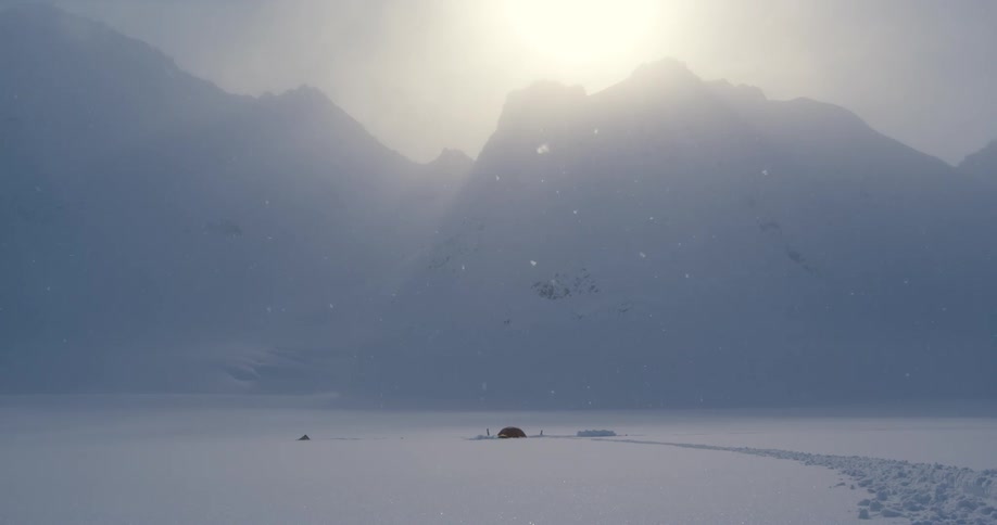 Snow falls over a small isolated hut built below mountains