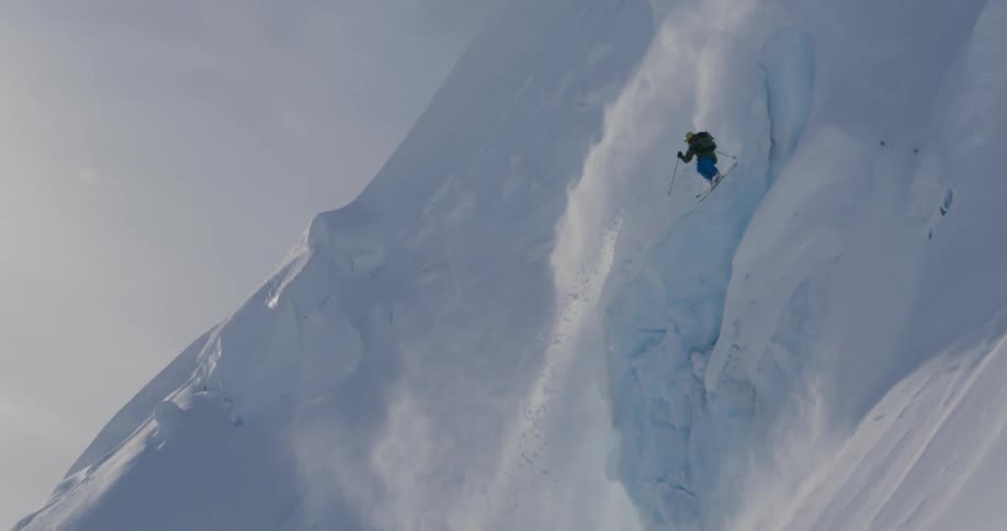 A person with a jacket and helmet skiing down a snow covered mountain with the sky in the background