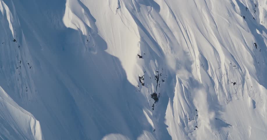 Skier in a red jacket slides down the steep snow covered slopes of a mountain