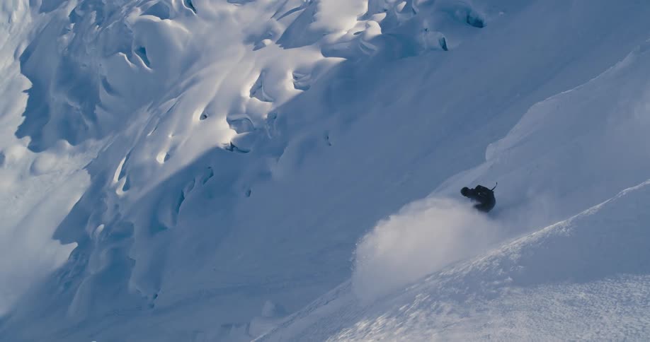 The sun shines down as a person skis down a snow covered mountain