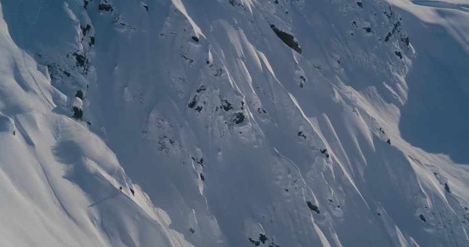 A skier descends a steep mountain slope on a sunny day
