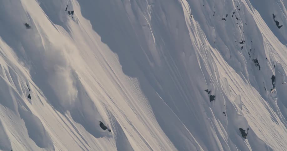 A snowboarder descends a steep mountain slope on a sunny day