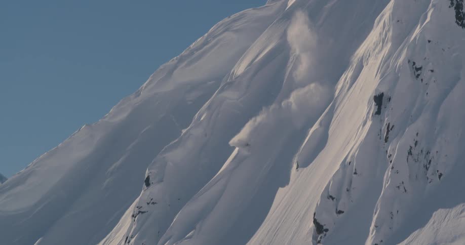 A person snowboarding down a mountain with the sky and clouds in the background