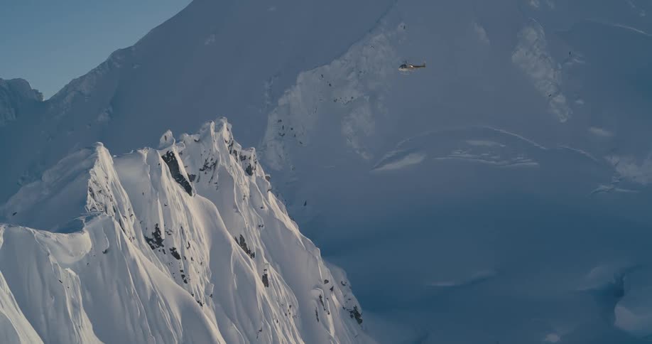 A helicopter flying over a snow covered mountain range turns around in midair and heads back the way it came