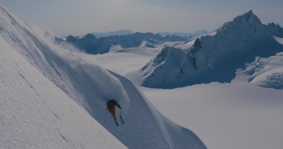 A skier descends the steep slope of a mountain on a sunny day