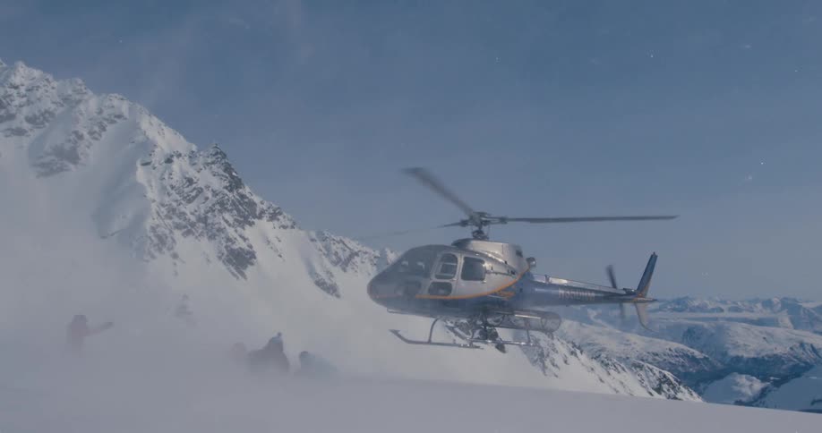 A helicopter landing on a mountain where a small group of people huddle together