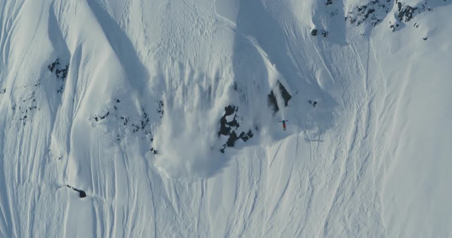 Skier skis down steep snowy slope taking a jump and causing a mini avalanche they need to evade