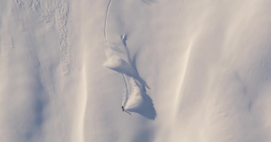 A person snowboarding down a snowy slope with sunlight and shadow