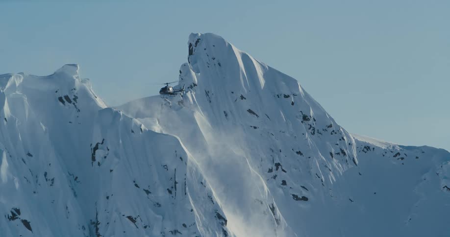 Helicopter hovers over steep mountain peaks covered with snow