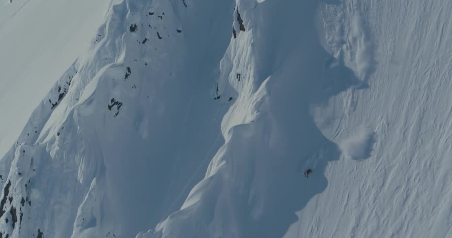 A skier descends a steep mountain slope on a sunny day