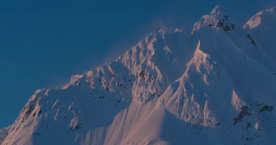 A rocky mountain range is almost completely covered in snow as sun light shines upon it