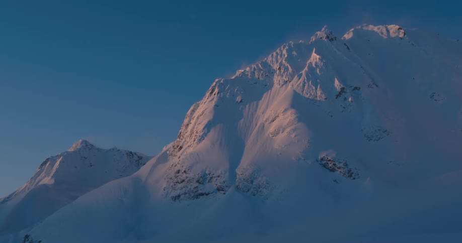 A mountain peak covered in snow under a clear evening sky