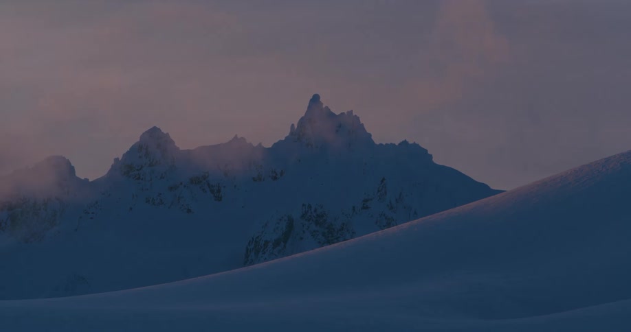 A jagged mountain ridge behind a snow covered slope