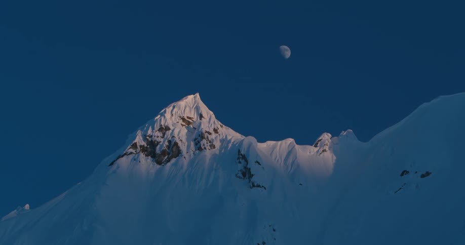 Moon rises above snow covered mountain peak