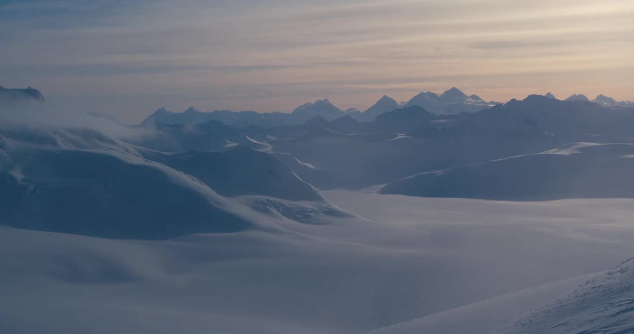 A pink hued sky above snow covered ridges and peaks