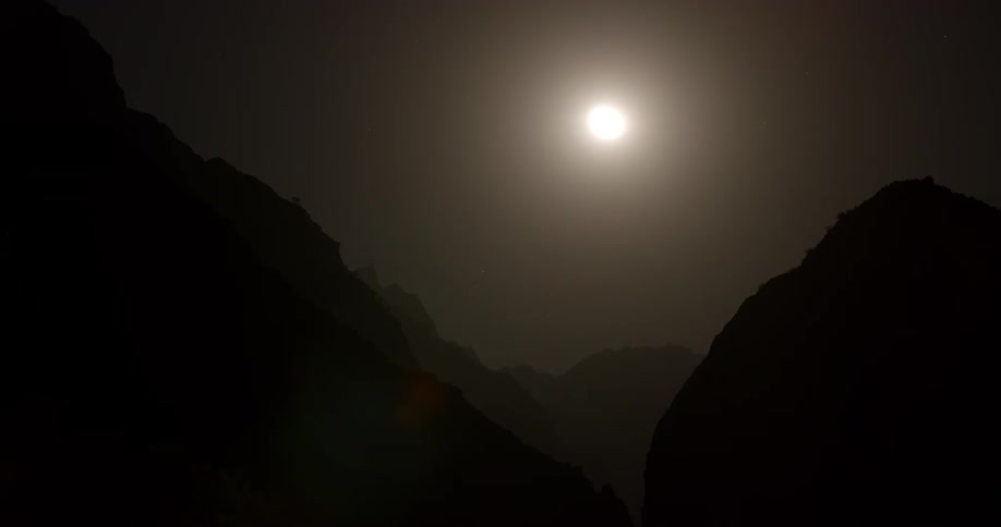 A silhouette of a mountain range with the sky the moon and stars in the background