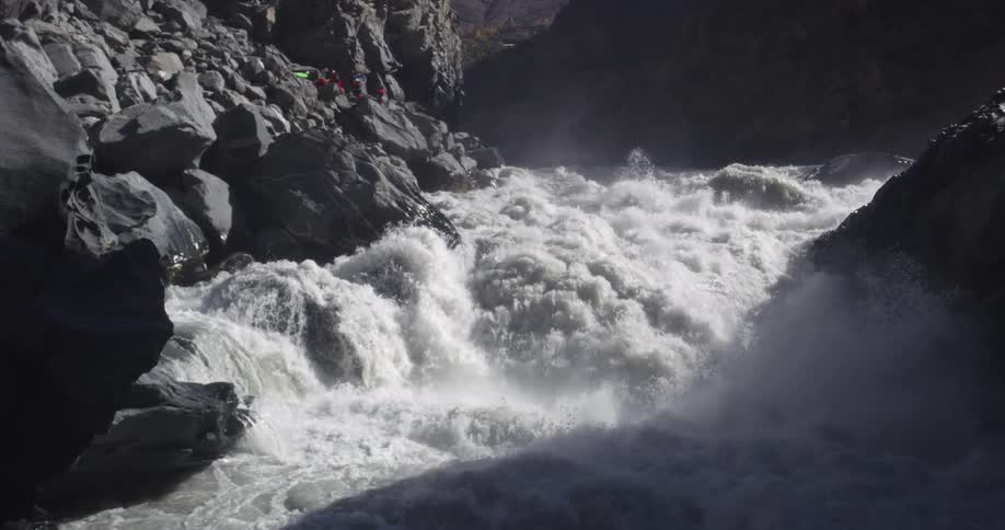 People with kayaks stand on a large rock and look at the river rapids