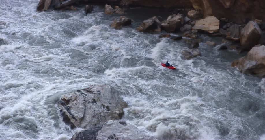 A kayaker attempts to control their kayak as it is washed down the violent rapids of a river