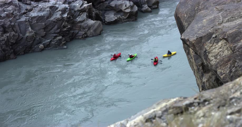 A group of kayakers travel together atop a river running through a canyon