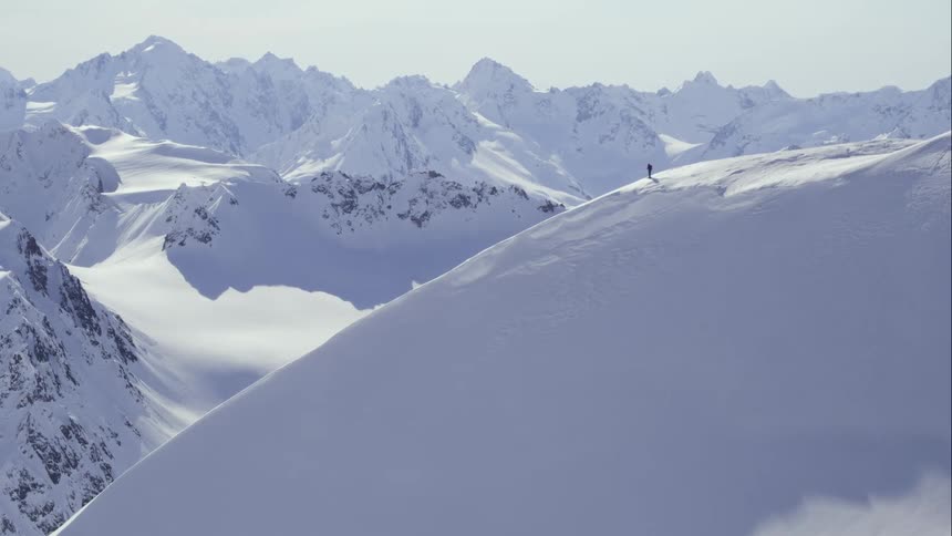Aerial of a person walking to top of mountain peak in snow covered mountain range